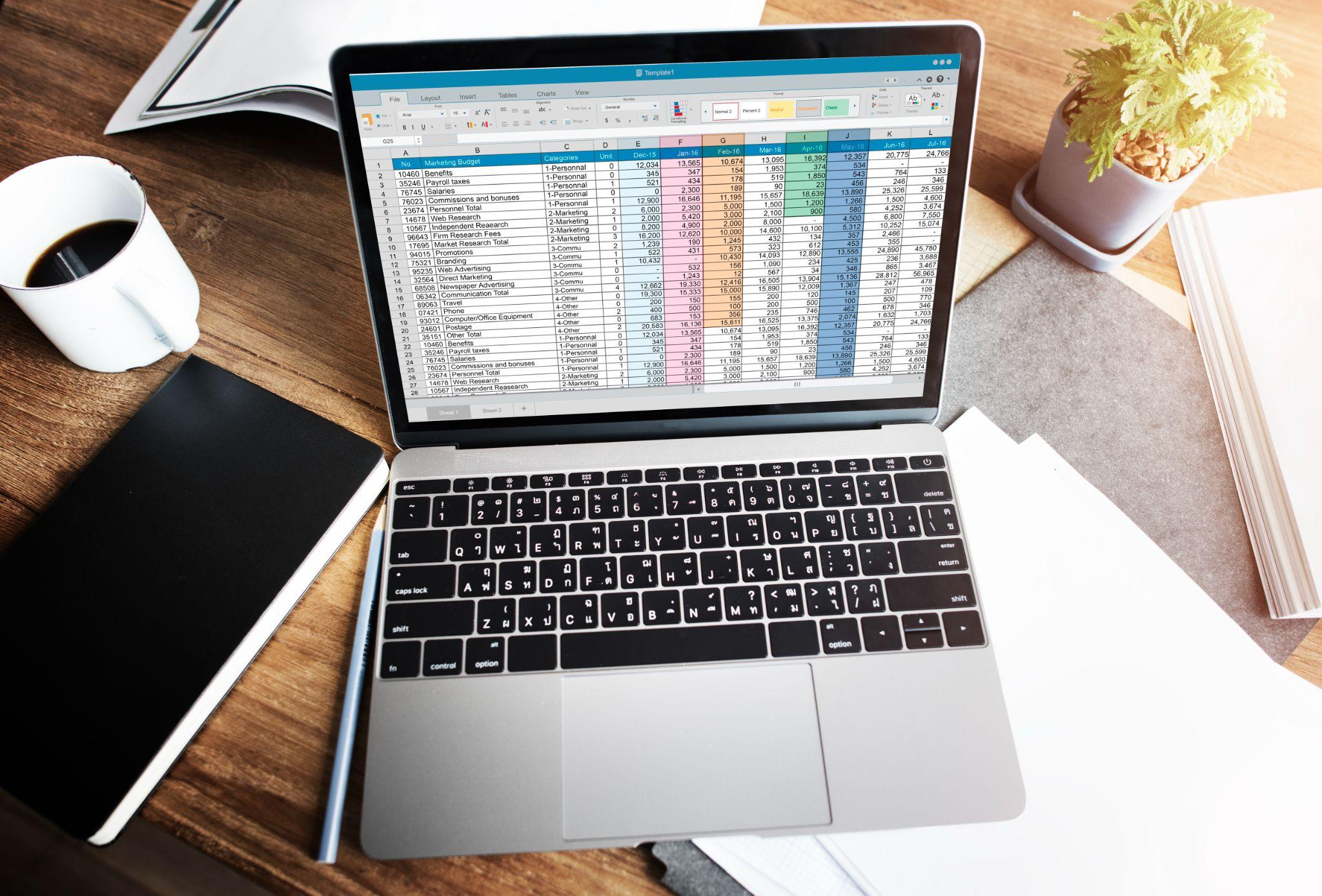 he Ultimate Guide to Buying Microsoft Office Online: Editions, Pricing, and Best Deals for 2024 1 shot of a laptop with an Excel sheet on display, placed in the center of a messy desk