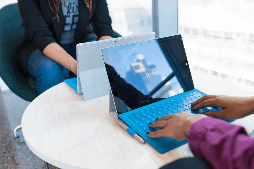 two people sitting at a round table using their Microsoft laptops